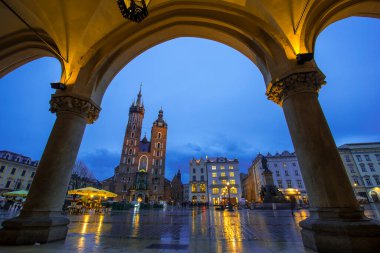 KRAKOW - POLAND - 01 Nisan 2019: St Mary Bazilikası (Mariacki Kilisesi) ve beyaz vagonlar Eski Krakow Kasabası 'ndaki Ana Pazar Meydanı' nda gece aydınlatıldı (Krakow))