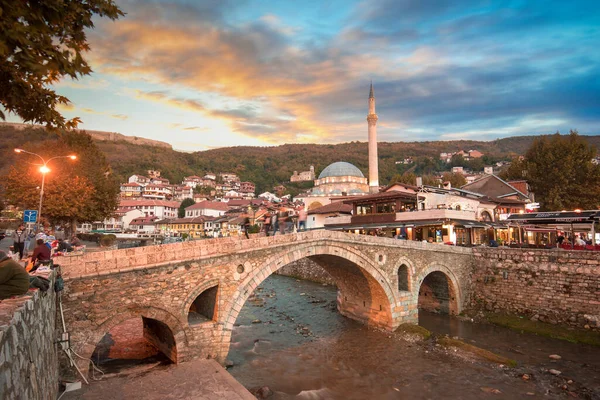 Prizren, Kosova - 08 Temmuz 2019: Eski taş köprü ve eski Osmanlı Sinan Paşa Camii 'nin günbatımı. Bistrica nehrinin kıyısında tarihi bir şehir.