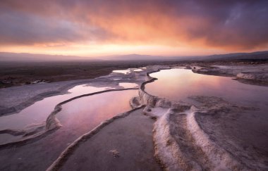 Pamukkale 'de güzel gün batımı ve doğal travertin havuzları ve terasları. Denizli yakınlarındaki Türkiye 'nin güneybatısındaki pamuk şatoda sıcak su, turkuaz mavisi bir su ile bembeyaz renklendiriliyor.