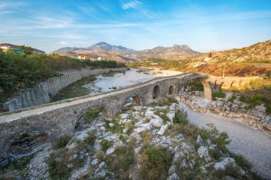 Arnavutluk 'un Mes kentindeki Mesi Köprüsü' nün (Ura e Mesit) Panoraması. Eski bir Osmanlı köprüsü - ülkenin en büyüğü. Güzel kuru nehir ve dağların manzarası.
