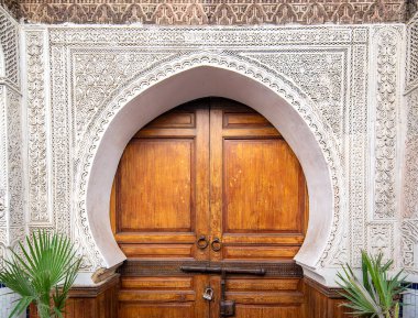 Traditional Moroccan style design of an ancient wooden entry door. In the old Medina of Fez. Typical, old, brown intricately carved, studded, Moroccan riad door clipart