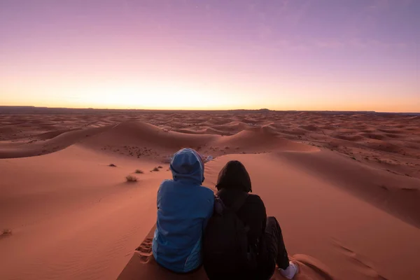 Aşk dolu bir çiftle gece manzarası. Kum tepelerinde oturmuş ufka bakan kız ve erkek. Sahra çölünde gün doğumu, Merzouga, Fas. Erkek ve kadın. Aşk kavramı