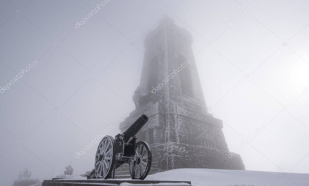 Shipka Monument (Monument of The Liberty) is a monumental construction, located at Shipka peak in Stara Planina mountain, near town of Shipka, Bulgaria at winter fog . artillery gun covered with snow