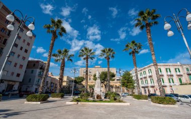 Monopoli, Puglia, İtalya - 01 Mart 2019: Meydanı ve heykeli olan sokak ve sokak. Eski kasabadaki renkli evler ve palmiyeler. Apulia Bölgesi