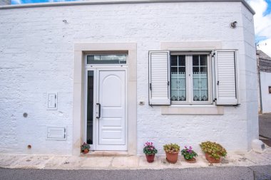 Beyaz duvardaki ahşap beyaz kapının önü. Çiçekli güzel kırmızı kaplar. Alberobello, Puglia, İtalya 'da bir evin dışında. Apulia Bölgesi