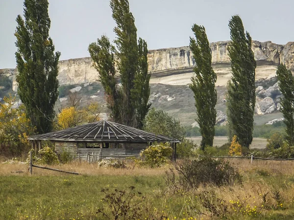 An old agricultural building on the background of the white cliffs of the Ak-Kaya mountain in the Crimea. Cloudy autumn day.