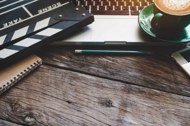 Film clapper laptop ve kahve Kupası kalem Not defteri ile vurdu ahşap masa üstü görünümünde başı işleri.