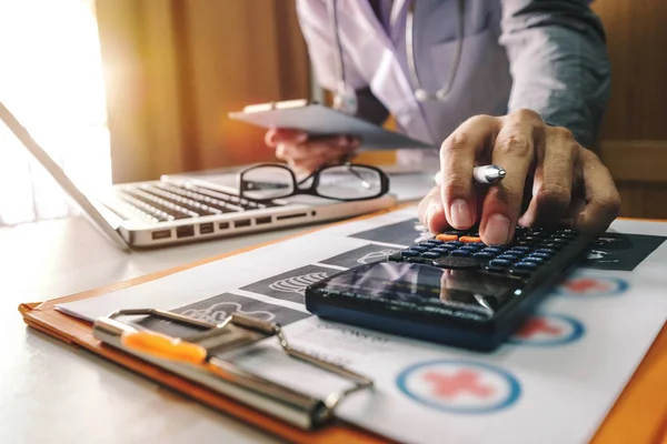 Healthcare costs and fees concept.Hand of smart doctor used a calculator and tablet for medical costs at modern hospital in sun light