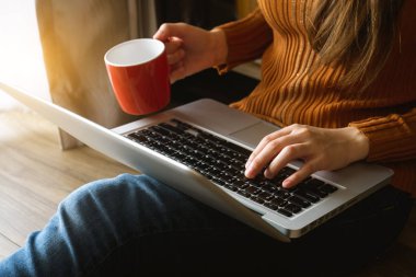 Kadın dizüstü bilgisayar kullanıyor ve dizüstü bilgisayarda daktilo kullanıyor ve kahve fincanı tutuyor.