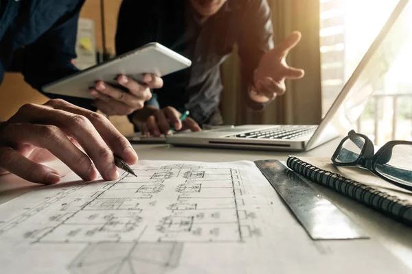 Two colleagues discussing data working and tablet, laptop with on on architectural project at construction site at desk in office