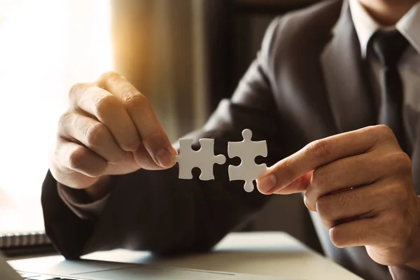 Business solutions and success concept. Businessman hand connecting jigsaw puzzle at office in morning light