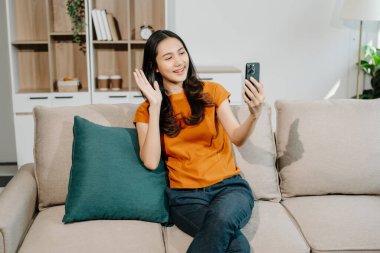 Genç Asyalı kadın evdeki kanepede dinleniyor ve akıllı telefondan selfie çekiyor.