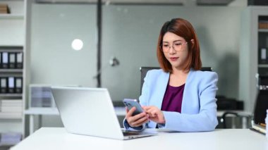 Ofis masasında otururken akıllı telefon kullanan genç iş kadını.