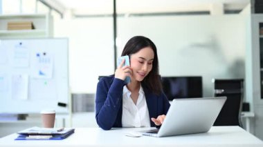 Dizüstü bilgisayarla çalışırken telefonda konuşan genç bir iş kadını.