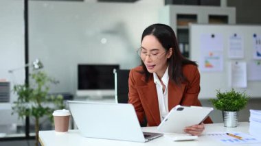 Çekici iş kadını masada dizüstü bilgisayar ve tablet kullanarak oturuyor.