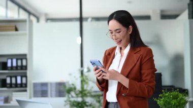 Modern ofiste akıllı telefon kullanırken gülümseyen iş kadını