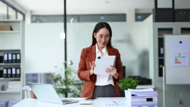 Modern ofis alanında ayakta dururken tablet kullanan kadın