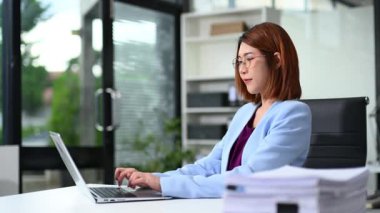 Modern ofis ortamında dizüstü bilgisayarda çalışan Asyalı iş kadını