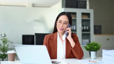 Masada otururken telefonda konuşan gülümseyen iş kadını.