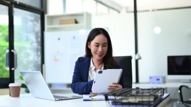 Genç iş kadını masada tablet kullanıyor ve mutlu bir şekilde gülümsüyor.