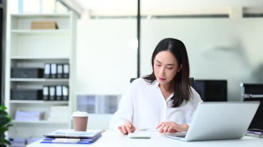 Masada oturan bir kadın dizüstü bilgisayarda çalışıyor.