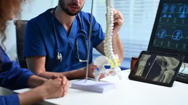 Doktor muayene sırasında hastaya omurga modelini açıklıyor.