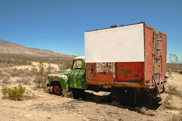 A wreckage of a red and green truck with a white large empty signboard in the desert, southwest usa.