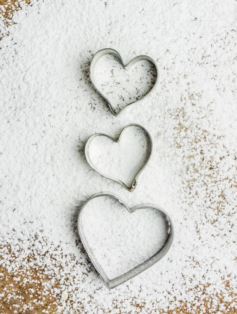Three heart shaped pastry cutter on a paste covered in icing sugar. These cutters are used to make traditional christmas cookies, Alsace, France - vertical