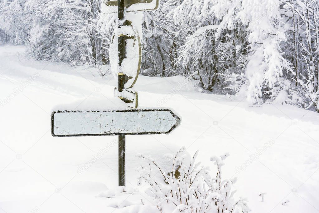 A blank direction sign covered in snow in a snowy environment while it's snowing