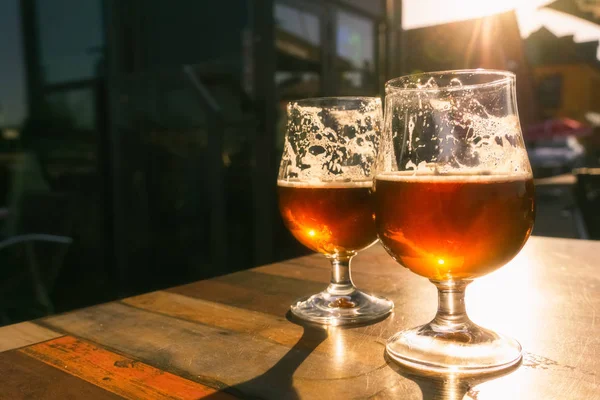 Großaufnahme von zwei Gläsern Bier auf einem Terrassentisch, durch den die Abendsonne scheint. Entspannung, Essen und Trinken mit Kopierraum. — Stockfoto