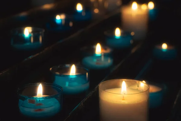 교회에서 푸른 유리 티 라이트에 불타는기도 촛불의 행의 클로즈업. 얕은 피사계 심도. — 스톡 사진