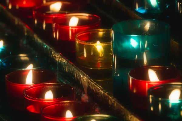 교회에서 여러 가지 빛깔의 유리 티라이트에 불타는 촛불의 행의 클로즈업. 선택적 초점. — 스톡 사진