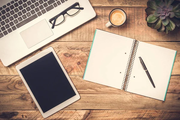 Laptop, computer tablet and open note book with white copy space on a rustic wooden table. Office work, workspace and desk top view concepts.