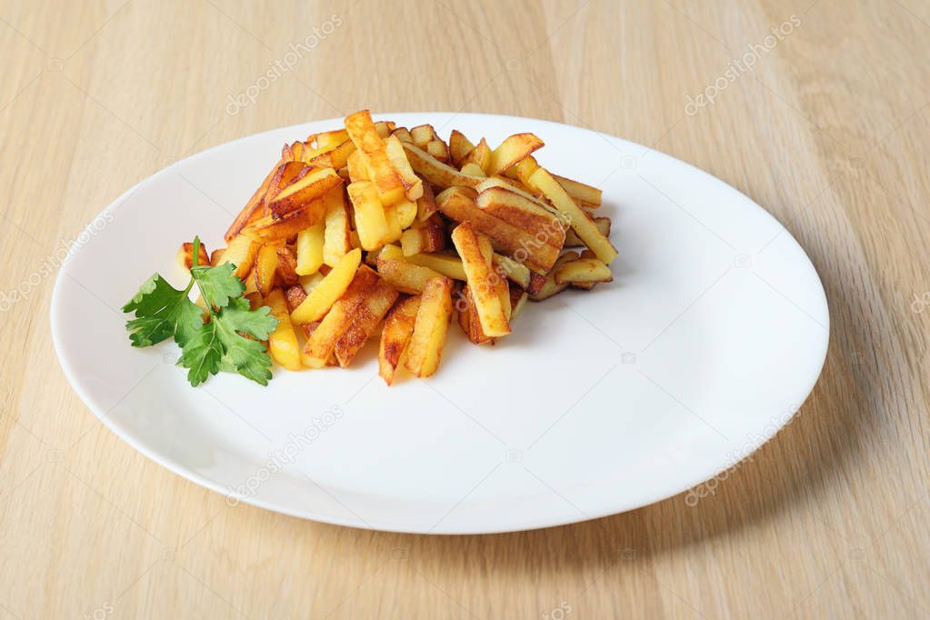 sliced fried potatoes on a white round dish on wooden table, side  view.