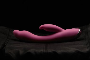 Siyah deride pembe yapay penis. Karanlık arka plan. Sanatsal aydınlatma.