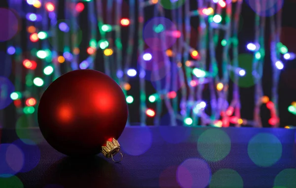 Rote Weihnachtskugel auf dunkel. aus dem Fokus Weihnachtsbeleuchtung Hintergrund. — Stockfoto