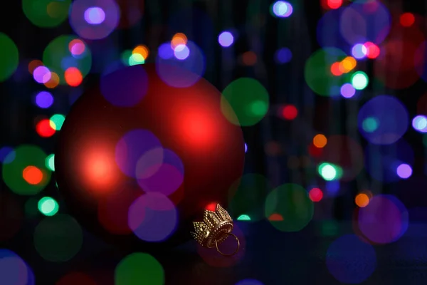 Bola de Natal vermelha no escuro. Fora de foco luzes de Natal fundo . Imagens De Bancos De Imagens