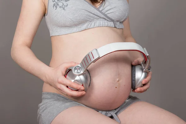 Ventre enceinte avec écouteurs sur fond gris neutre — Photo