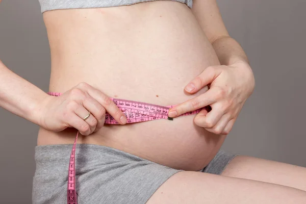 Een buik van zwangere vrouw meting van tape op neutrale grijze achtergrond — Stockfoto