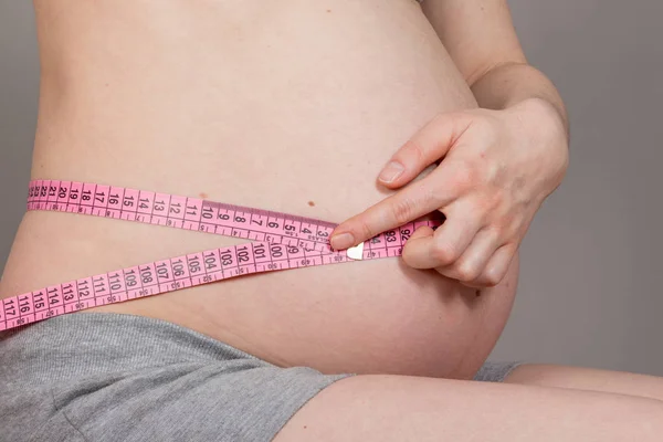 ニュートラルグレーの背景にテープの妊婦測定の腹 — ストック写真