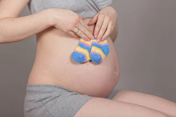 Schwangerschaftsbauch mit Socken auf neutralem grauen Hintergrund — Stockfoto