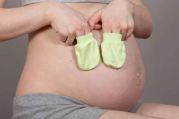 Vientre embarazada con manoplas sobre fondo gris neutro —  Fotos de Stock