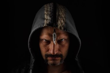 Koyu bir arka plan üzerinde bıyık ve sakal ile kapüşonlu Acımasız adam