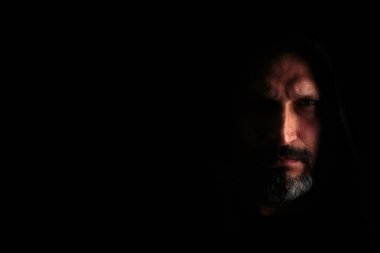 Kapüşonlu gri sakallı, siyah arka planda keskin gölgeleri olan acımasız bir adam. Kopyalama alanı.
