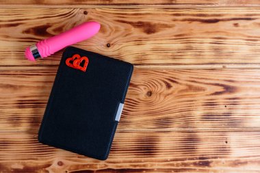 Ahşap arka plan üzerinde iki kalp ve pembe vibratör ile durumda Elektronik kitap. Romantik kitap konsepti.