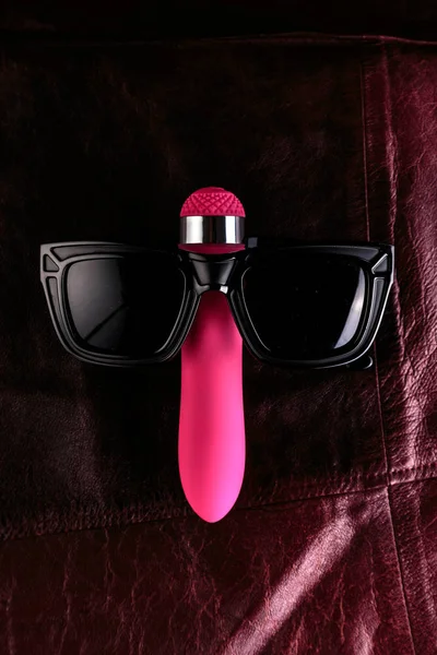 Vibrador rosa en gafas de sol sobre un fondo de cuero rojo. Sr. Cooldick . —  Fotos de Stock