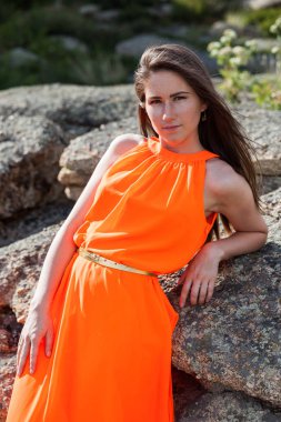 Dışarıda turuncu uzun elbiseli genç bir kadın var.