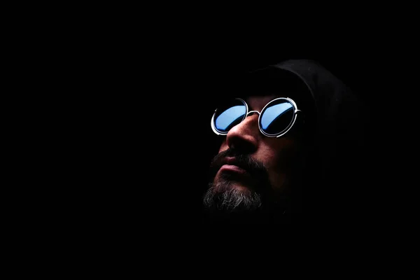 Жестокий человек в солнцезащитных очках, с бородой, в капюшоне на тёмном фоне. Надежда . — стоковое фото