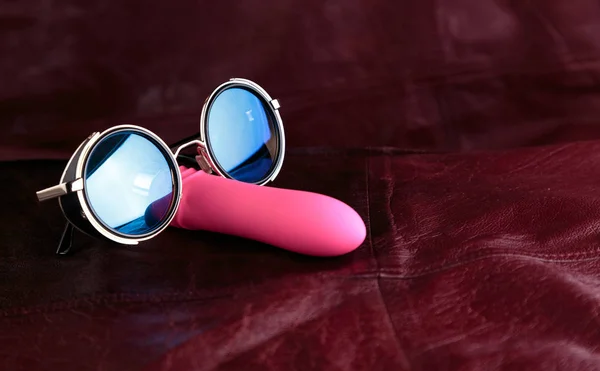 Kırmızı deri arka planda güneş gözlüğü pembe vibratör. Bay Cooldick.