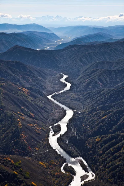 Il paesaggio di un fiume tortuoso che si estende oltre l'orizzonte, così come le montagne coperte di alberi e calotte di neve . — Foto Stock